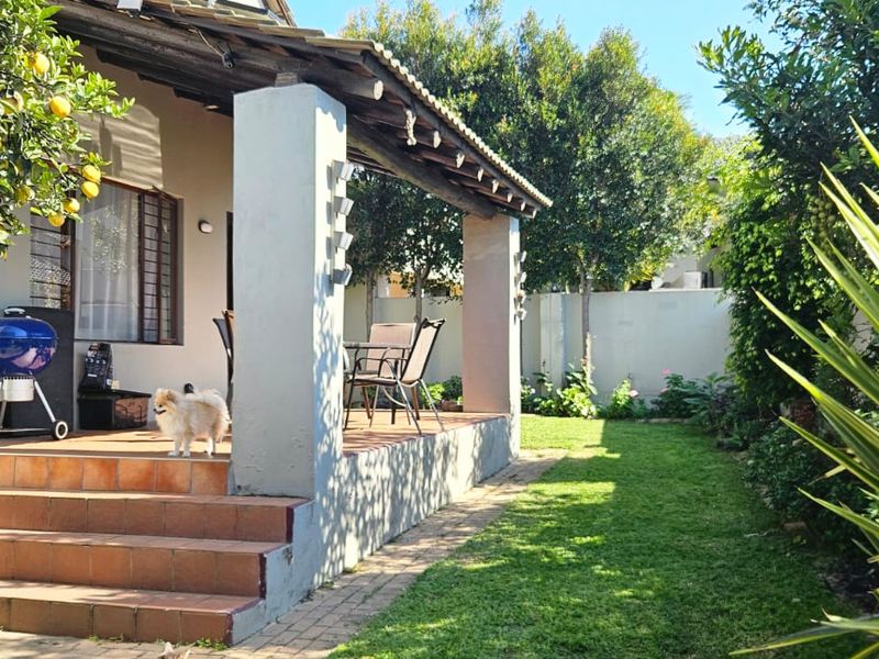 A covered outdoor patio featuring tiled flooring, concrete support pillars, and a timber roof structure, overlooking a private garden area.