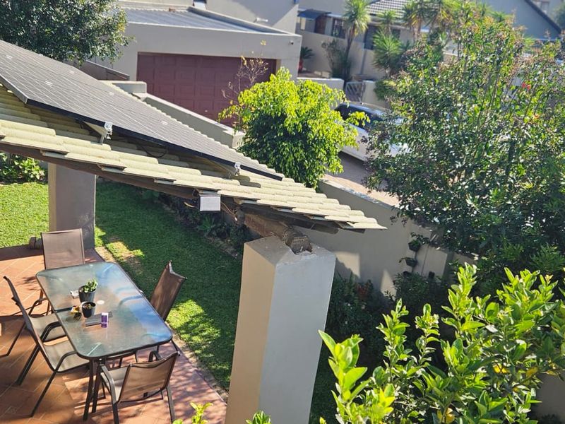 A covered patio area featuring tiled flooring and concrete support pillars, with solar panels installed on the roof structure.