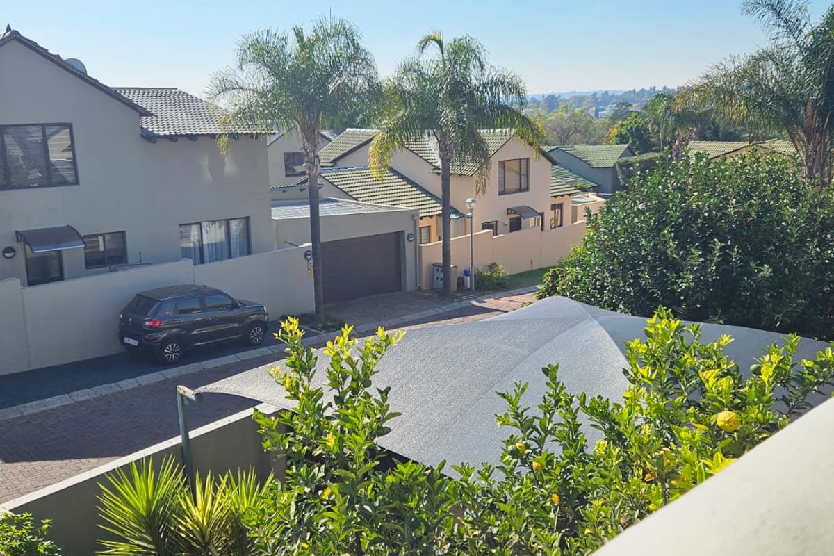 An elevated view of the property exterior showing the paved driveway, boundary walls, and a shade sail structure in a residential setting.