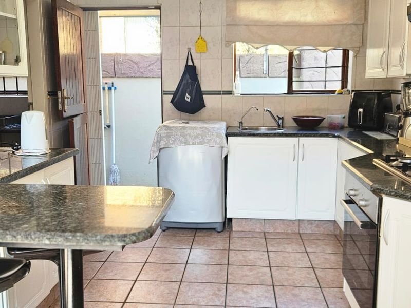 Functional kitchen featuring granite countertops, built-in oven, gas hob, extractor fan, and tiled finishes with direct access to an outdoor area.