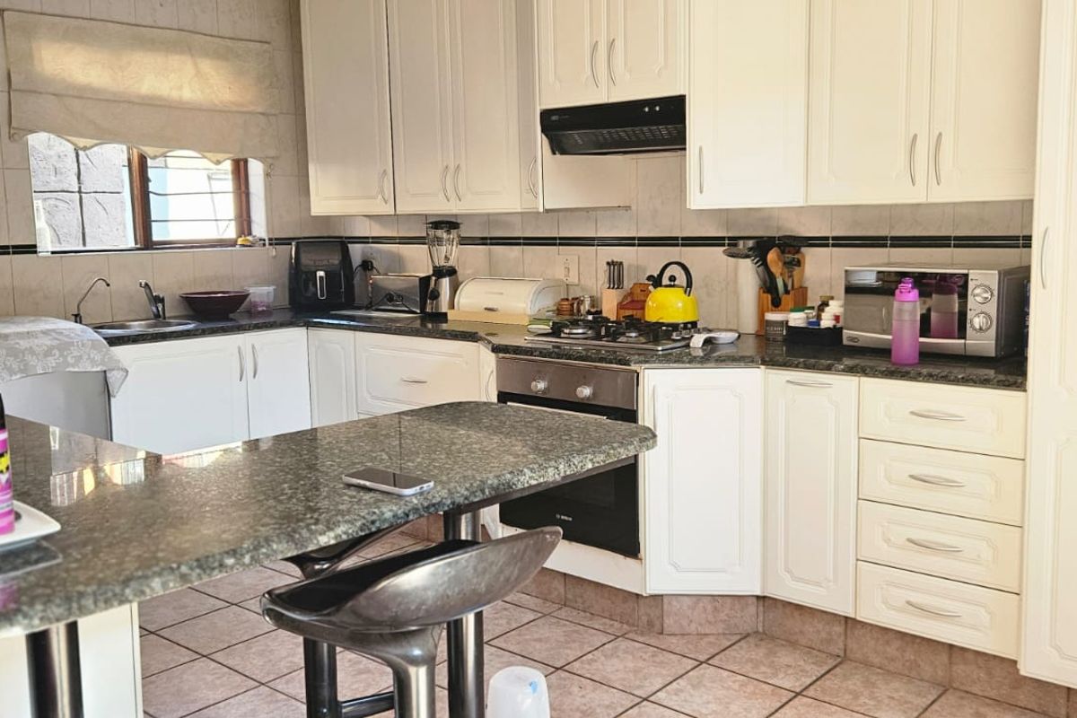 A functional kitchen featuring white cabinetry, granite countertops, a gas hob, built-in oven, and tiled flooring with a breakfast nook area.