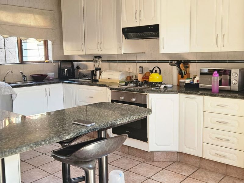 A functional kitchen featuring white cabinetry, granite countertops, a gas hob, built-in oven, and tiled flooring with a breakfast nook area.