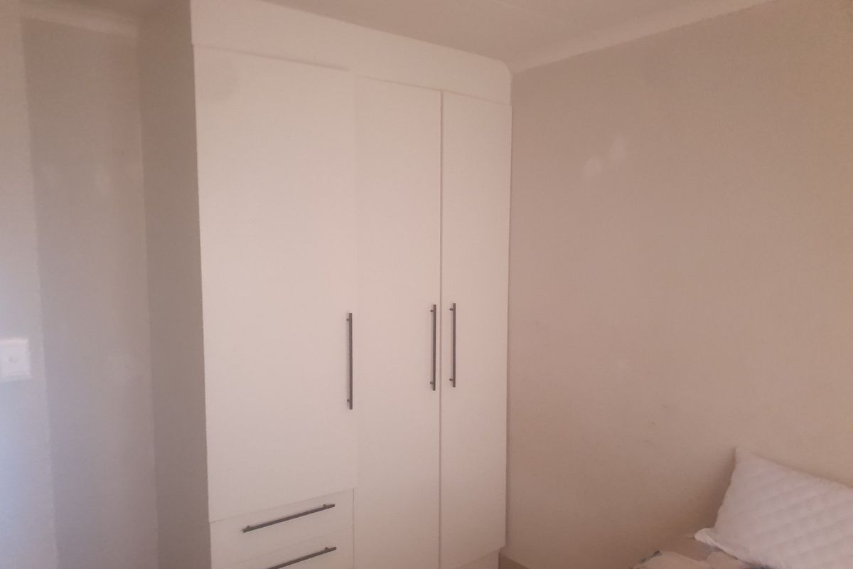 A bedroom featuring a white built-in wardrobe with integrated drawers and modern handles.