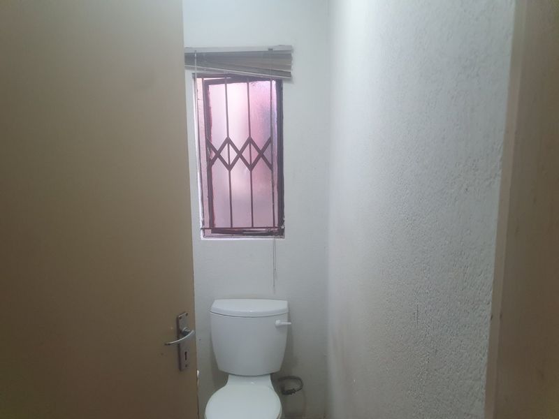 A compact, functional bathroom featuring a standard toilet and a window with security bars and a blind.