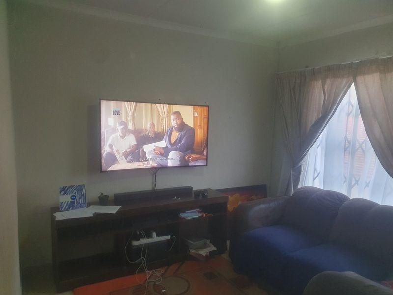 A living room featuring a wall-mounted television, curtained window with security gate, and neutral wall finishes.