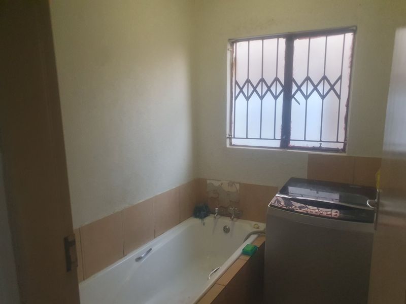 A small bathroom featuring a bathtub and tiled splashback, currently showing signs of wear and requiring maintenance to the wall finishes and window frame.