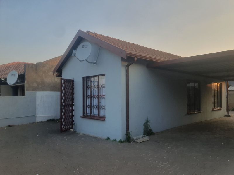 Front exterior view of the house featuring a paved driveway, attached carport, tiled roof, and security features on windows and doors.