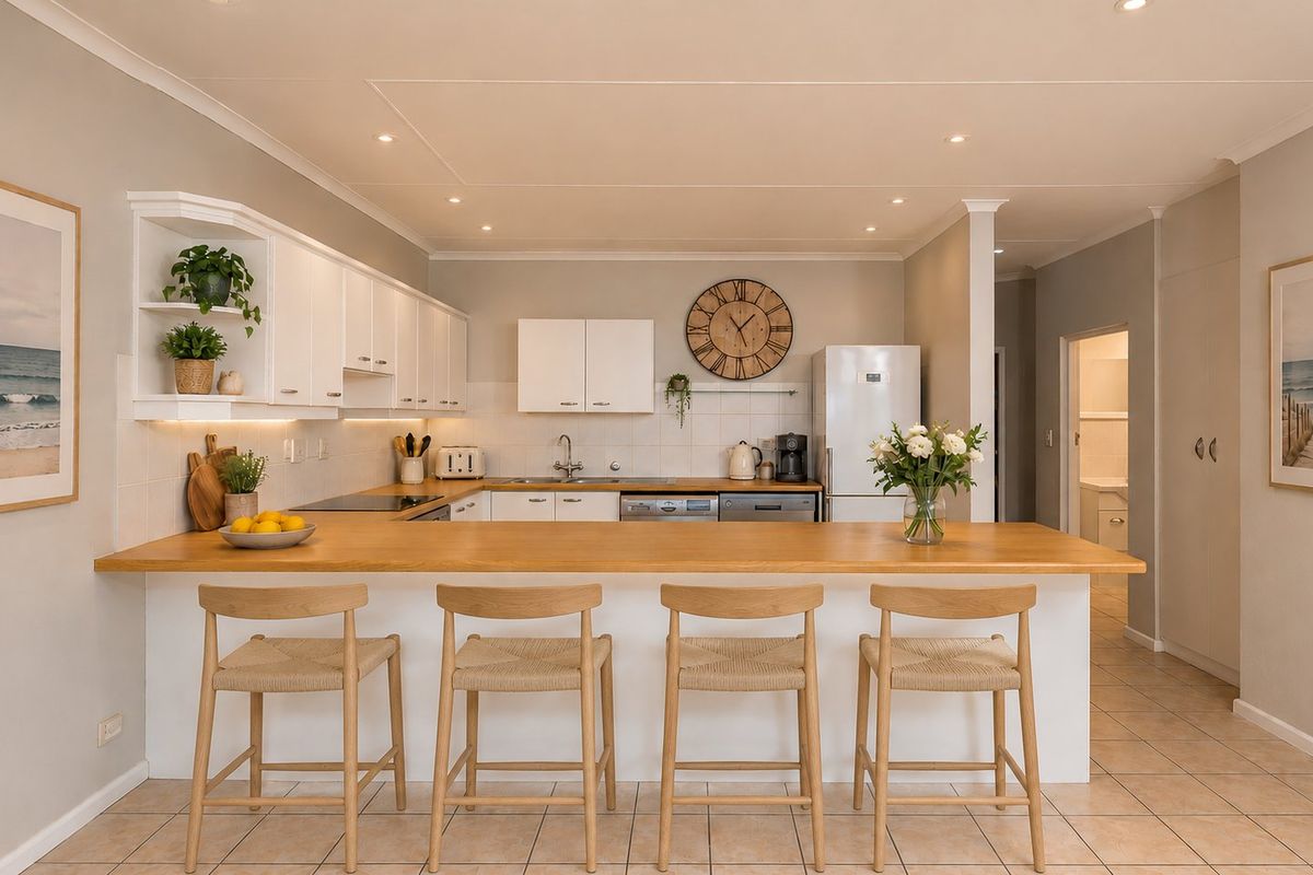 A bright, well-maintained kitchen featuring white cabinetry, a wooden breakfast bar, tiled backsplash, and recessed lighting, offering a clean and functional cooking space.