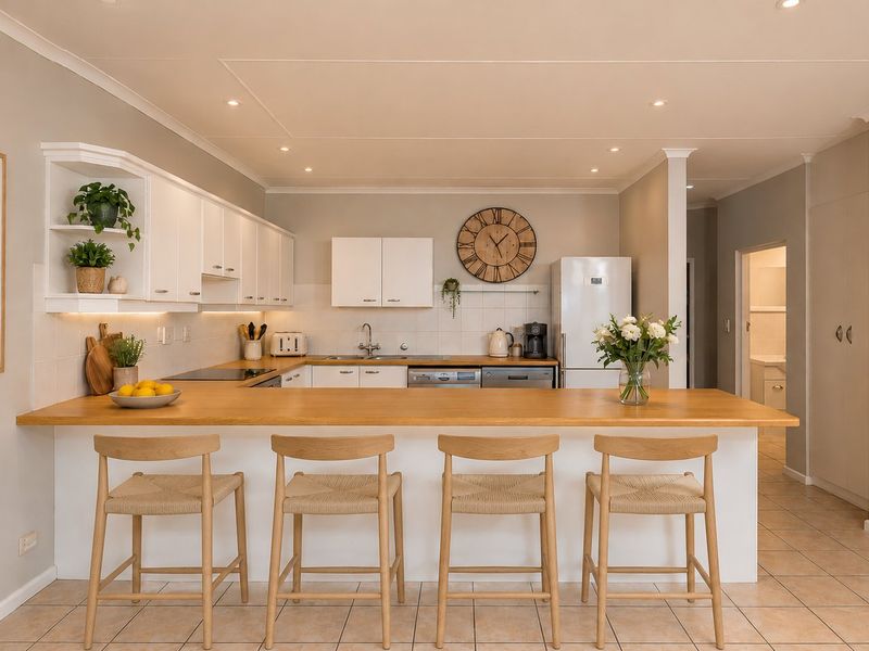 A bright, well-maintained kitchen featuring white cabinetry, a wooden breakfast bar, tiled backsplash, and recessed lighting, offering a clean and functional cooking space.