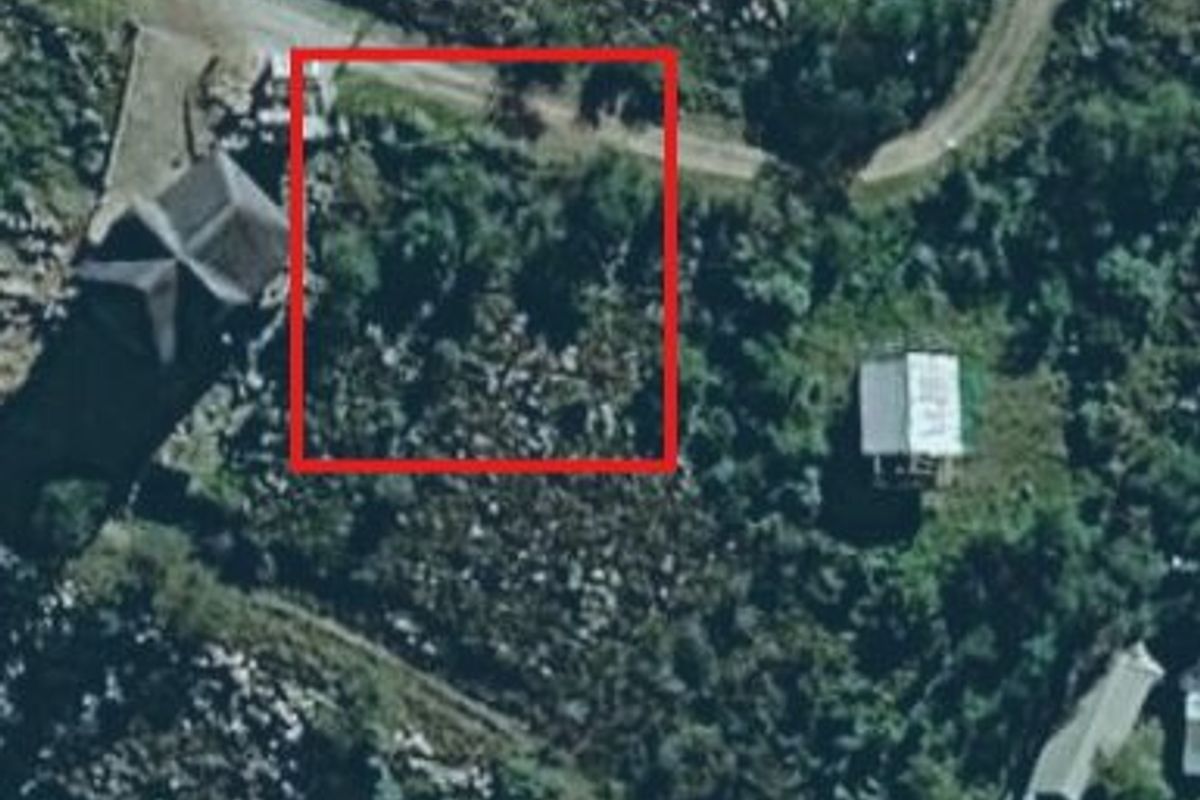 An aerial view of a vacant residential plot marked with a red boundary, surrounded by natural vegetation and nearby structures.
