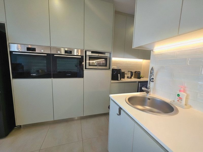 Modern kitchen featuring handleless cabinetry, integrated stainless steel appliances, subway tile backsplash, and under-cabinet lighting with a clean, contemporary finish.