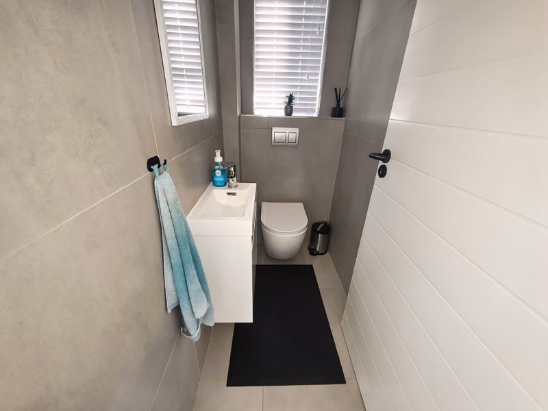 A modern, compact guest bathroom featuring a wall-hung toilet with a concealed cistern, a sleek vanity basin, and contemporary grey wall tiling.