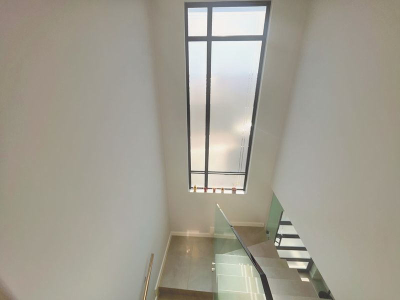 A bright, modern staircase area featuring a glass balustrade, metal handrail, and a large vertical window that provides ample natural light.
