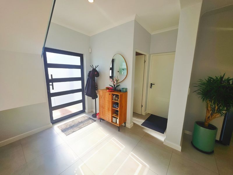 A bright and welcoming entrance hall featuring large format floor tiles, a modern glass-paneled front door, and clean, neutral wall finishes.