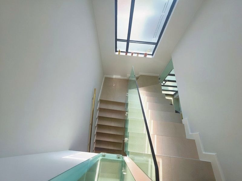 A bright, modern staircase featuring tiled steps, a sleek glass balustrade, and a large overhead skylight providing ample natural light.