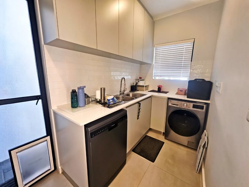 A modern, functional laundry room featuring sleek cabinetry, subway tile backsplash, stainless steel sink, and integrated appliances including a dishwasher and washing machine.