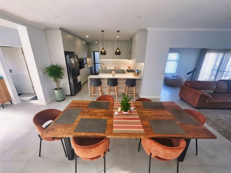 Modern open-plan living area featuring a contemporary kitchen with a central island, sleek cabinetry, and integrated appliances, flowing into a spacious dining and lounge area.