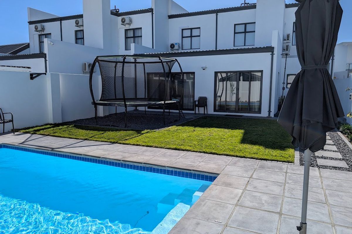 Rear exterior view featuring a swimming pool with tiled surround, a manicured lawn, and modern white building facade with sliding glass doors.