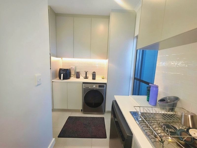 A modern, well-lit scullery featuring sleek built-in cabinetry, stone countertops, a subway tile backsplash, and an integrated washing machine.