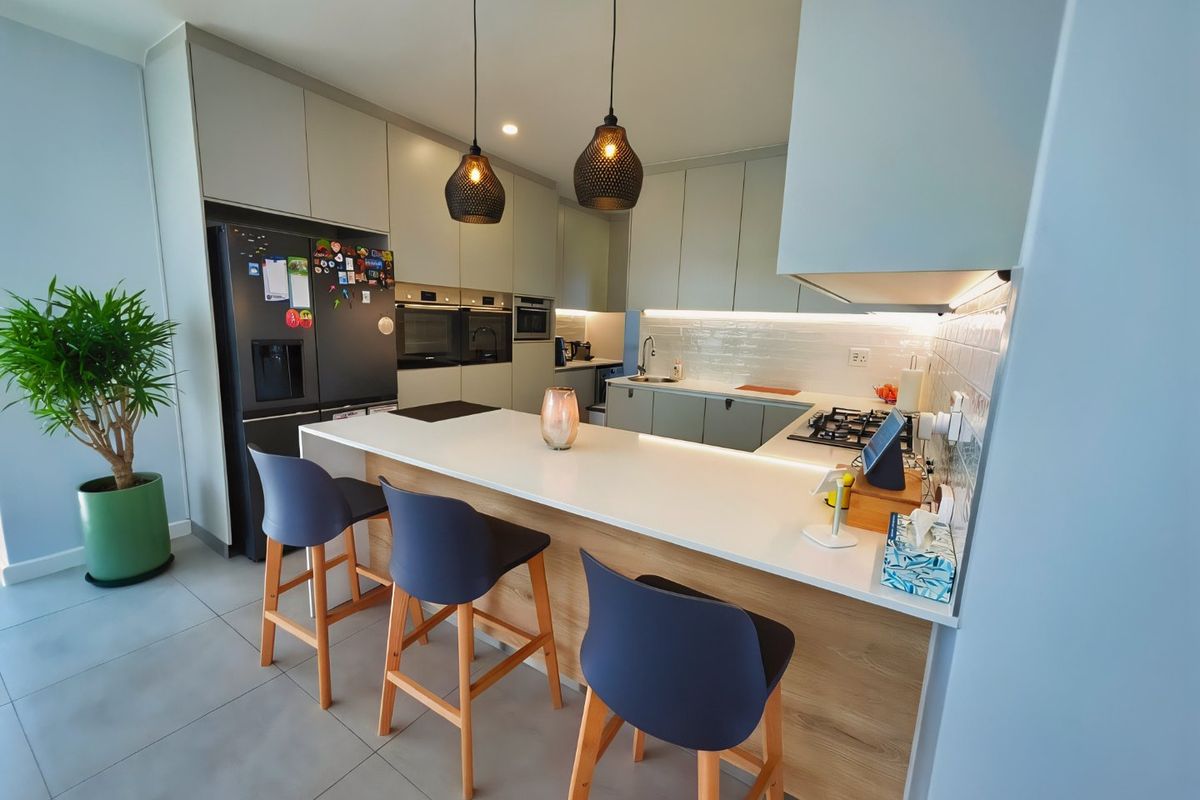Modern kitchen featuring sleek cabinetry, stone countertops, a central island with breakfast bar, and integrated appliances with under-cabinet lighting.