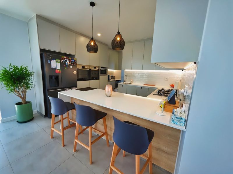 Modern kitchen featuring sleek cabinetry, stone countertops, a central island with breakfast bar, and integrated appliances with under-cabinet lighting.