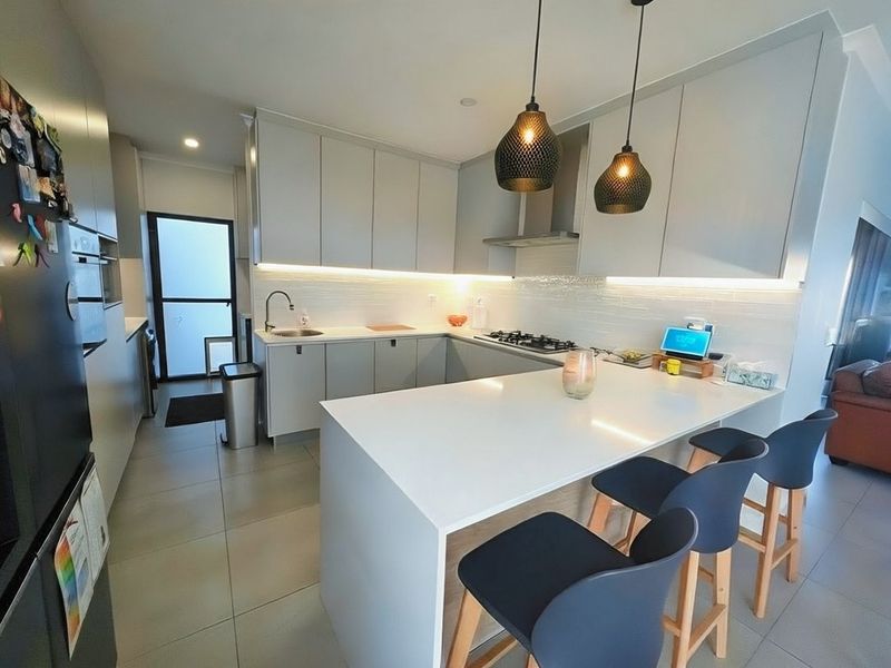 Modern kitchen featuring sleek grey cabinetry, stone benchtops, gas cooktop, and a breakfast bar with pendant lighting, creating a functional and contemporary culinary space.