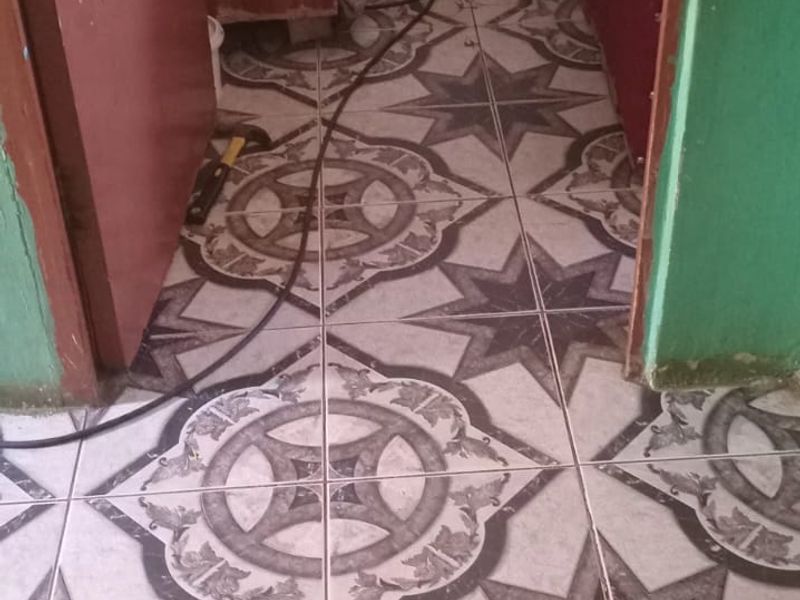 A narrow hallway featuring patterned ceramic floor tiles, showing signs of wear and exposed wiring near the doorway.