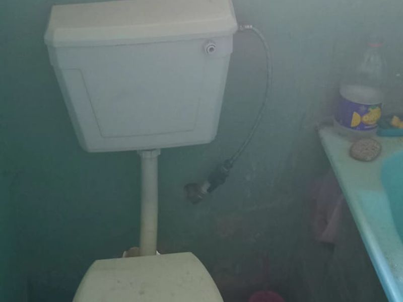A small bathroom featuring a standard toilet and vanity basin with patterned floor tiles and painted walls requiring maintenance.