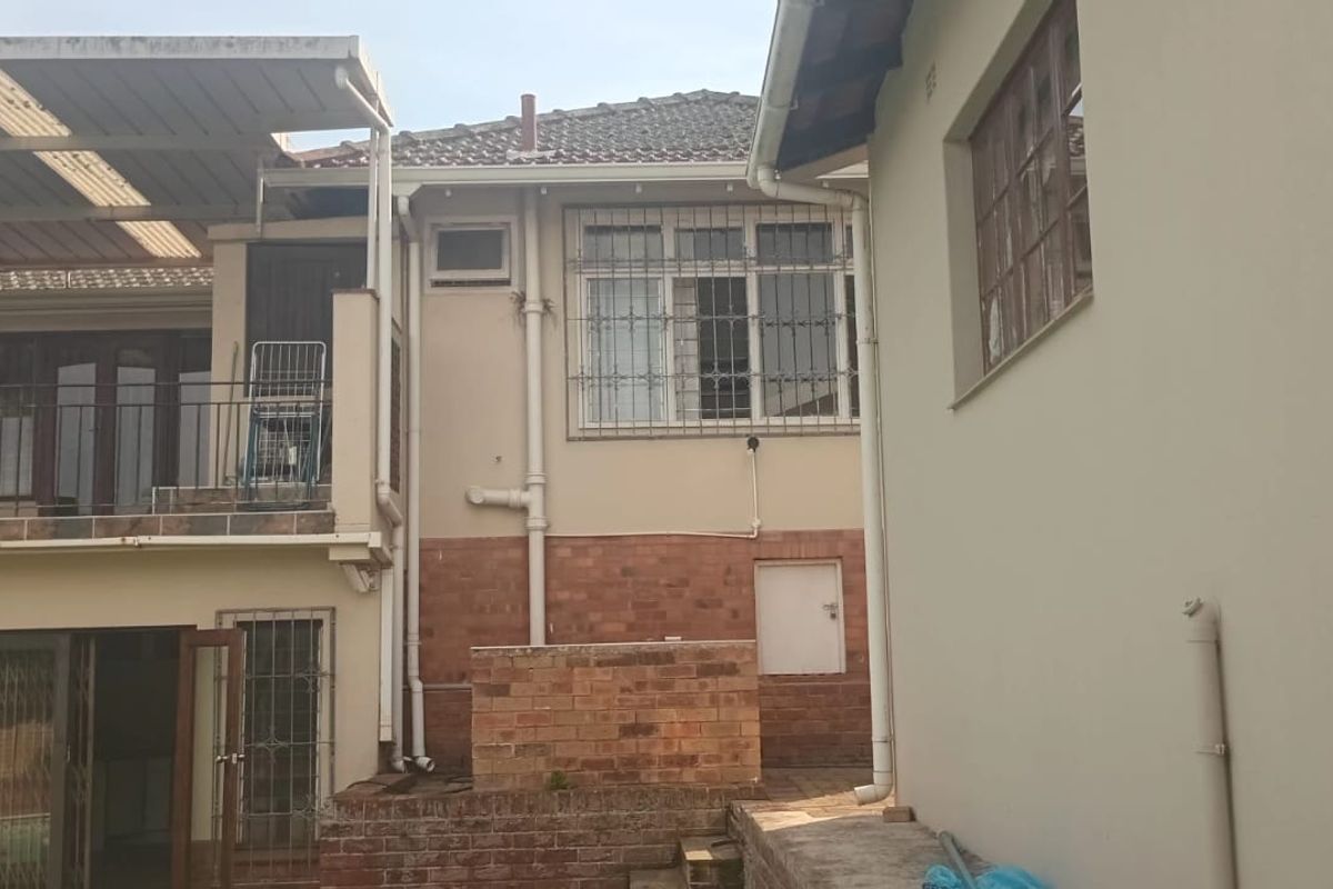 Rear exterior view of the house featuring a covered patio, brick retaining walls, and security-fitted windows.