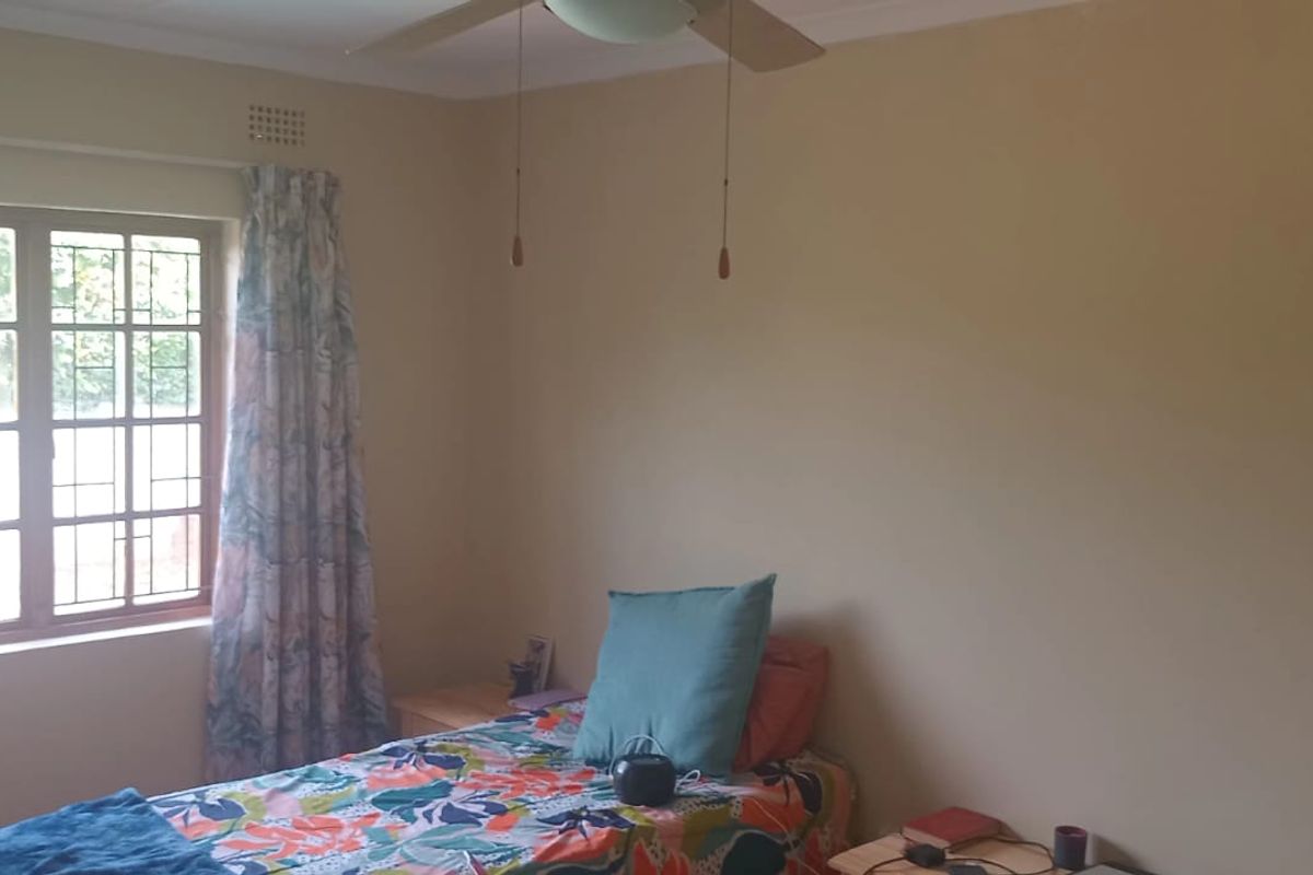 A standard bedroom featuring a ceiling fan and a window with security bars, providing a functional and neutral living space.