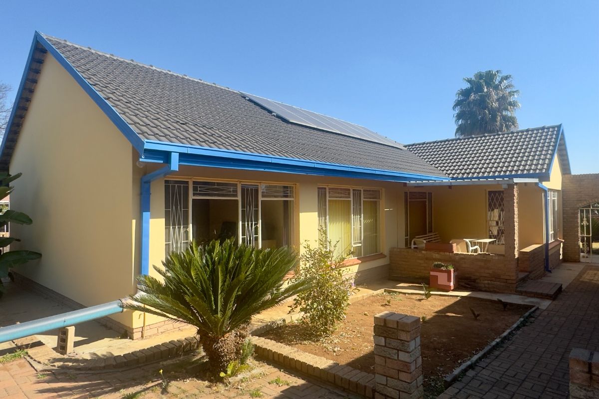 Rear view of the house featuring a tiled roof with solar panels, paved courtyard, and a covered patio area.