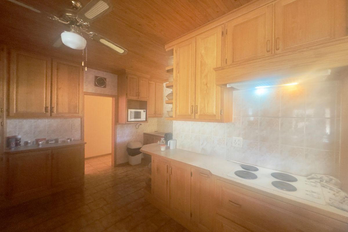 A traditional kitchen featuring extensive wooden cabinetry, a built-in electric hob with extractor fan, tiled backsplash, and a distinctive wooden ceiling.