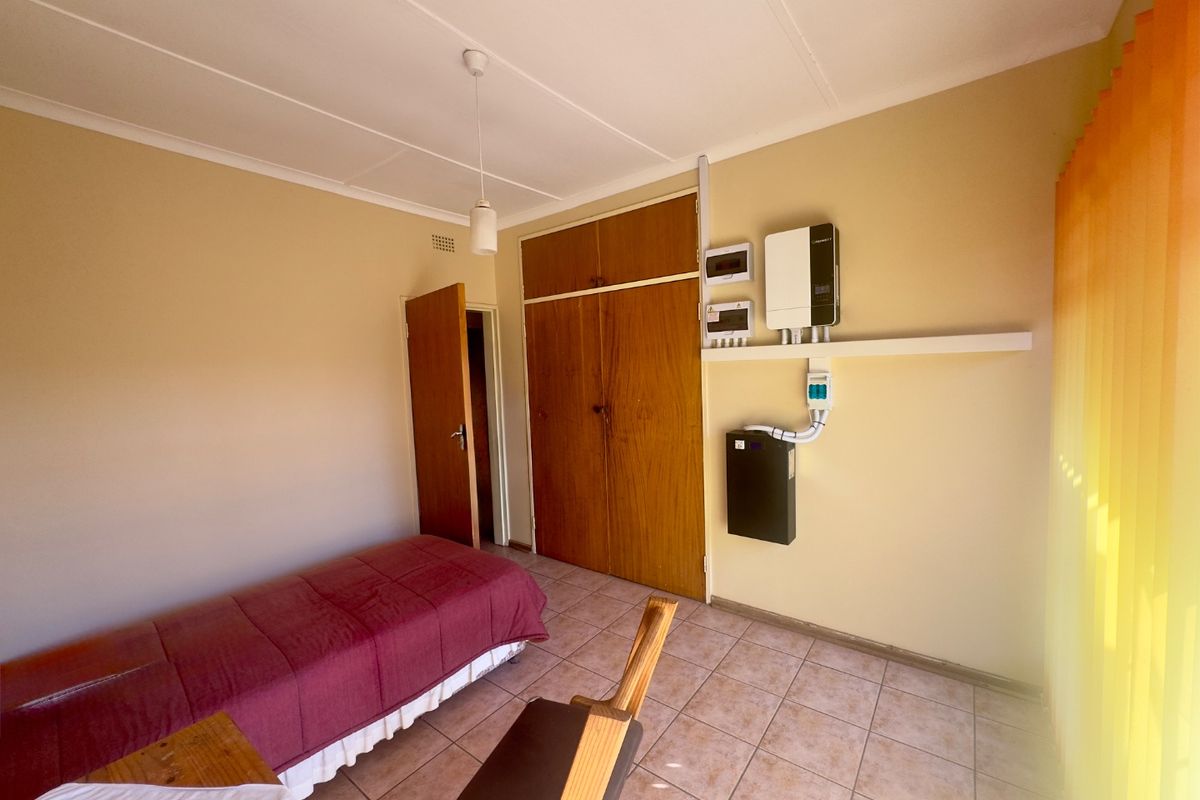 Bedroom featuring tiled flooring, built-in wooden cupboards, and a wall-mounted inverter and battery system for backup power.
