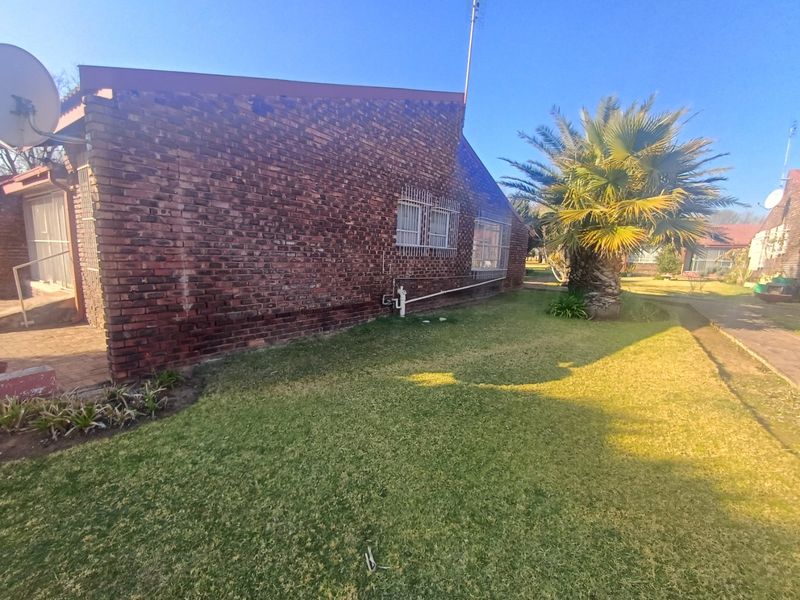 A view of the rear exterior of the townhouse featuring face brick walls, security bars on windows, and a landscaped garden area.