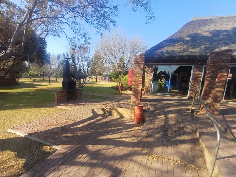 Outdoor patio area featuring brick paving, a built-in braai, and access to the garden through sliding glass doors under a thatched roof structure.