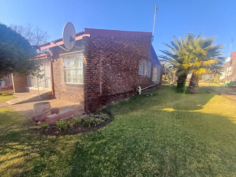 Rear view of a face brick townhouse featuring a paved patio area, security bars on windows, and a well-maintained garden with a palm tree.