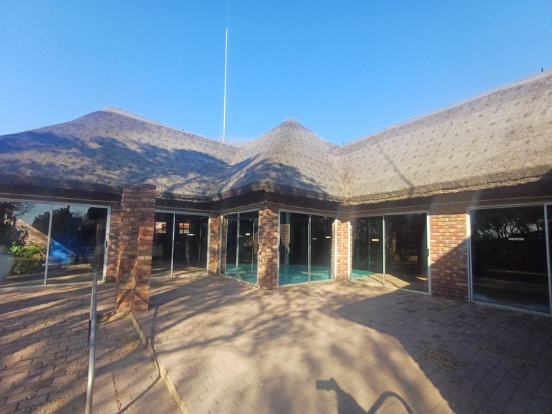 Rear exterior view of a townhouse featuring a traditional thatch roof, face brick construction, and extensive sliding glass doors opening onto a paved patio area.