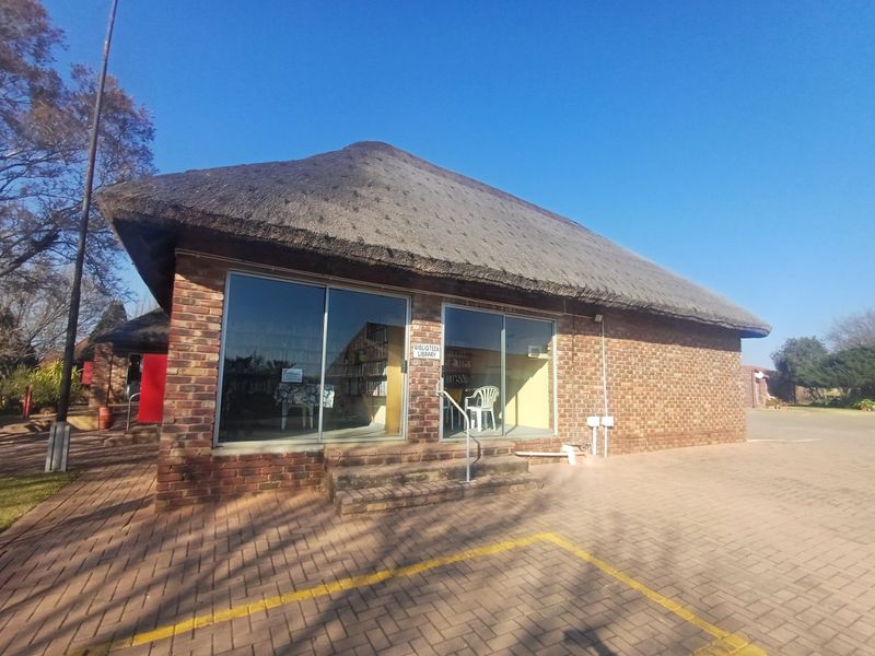 Exterior view of a face brick clubhouse building featuring a traditional thatch roof and large sliding glass doors, situated on a paved lot.