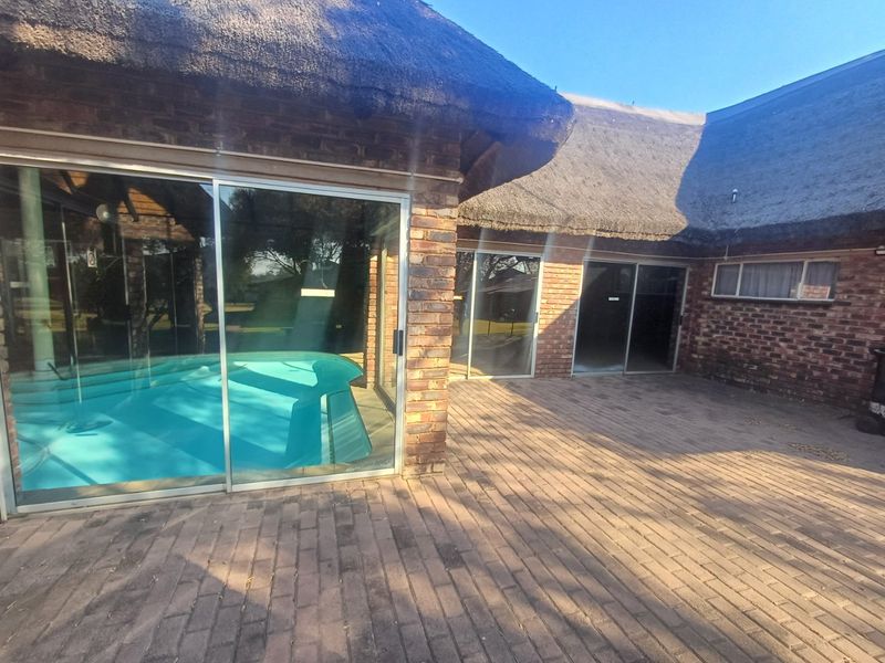Rear exterior view of a townhouse featuring a paved patio, swimming pool, and traditional thatch roof with sliding glass door access.