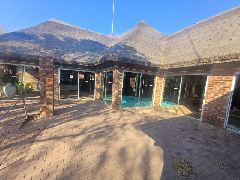 Spacious paved patio area featuring exposed brick pillars and large sliding glass doors, covered by a traditional thatched roof structure.