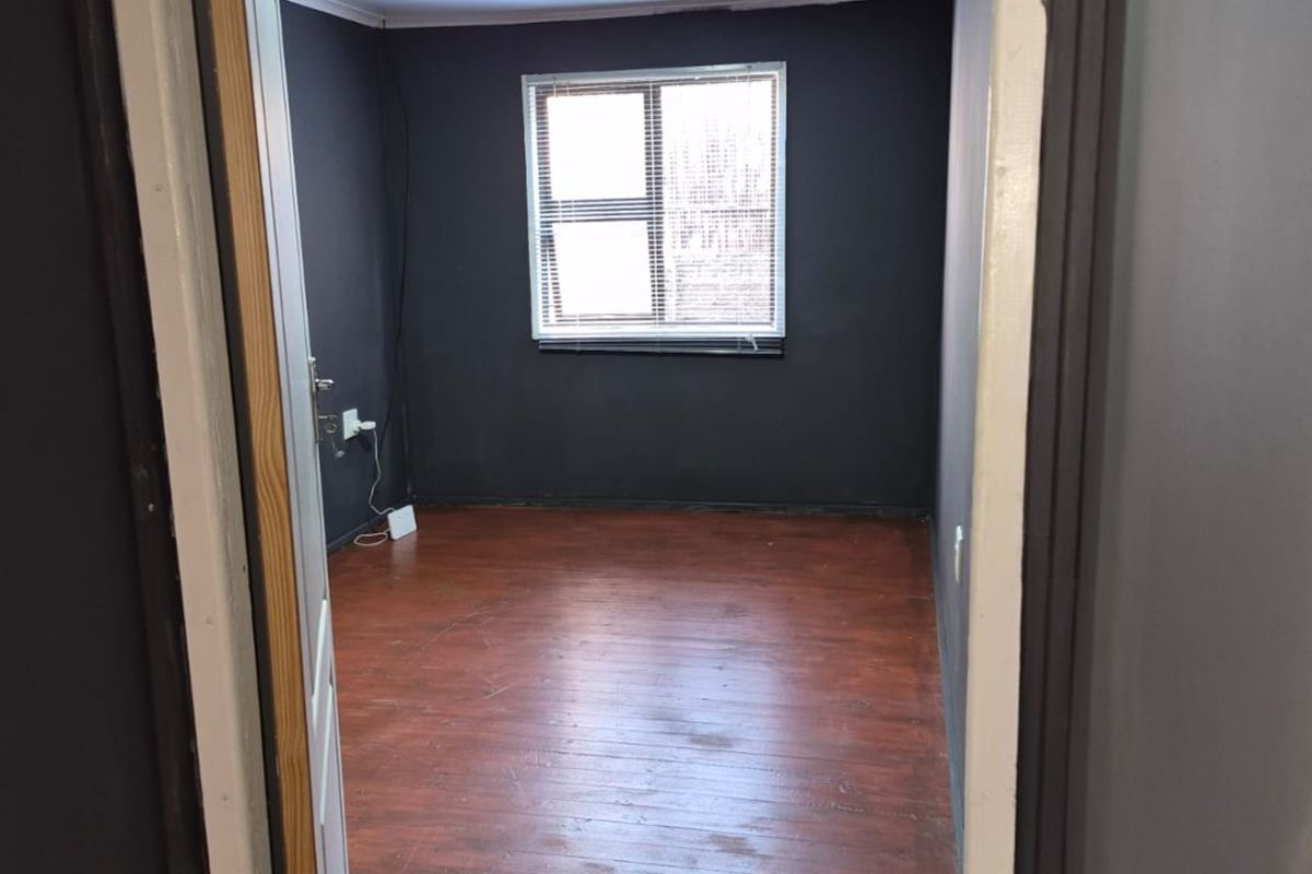 An empty bedroom featuring dark painted walls, laminate flooring, and recessed ceiling lighting, presenting a blank canvas for potential renovation or staging.