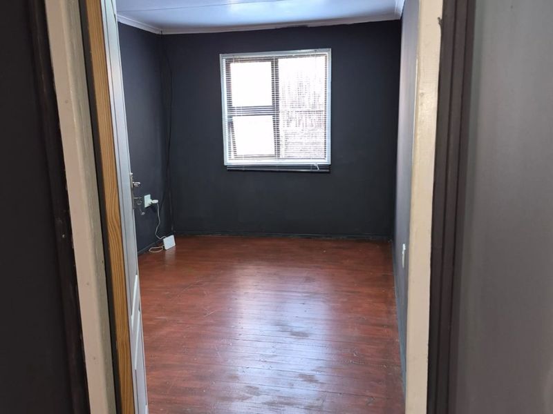 An empty bedroom featuring dark painted walls, laminate flooring, and recessed ceiling lighting, presenting a blank canvas for potential renovation or staging.