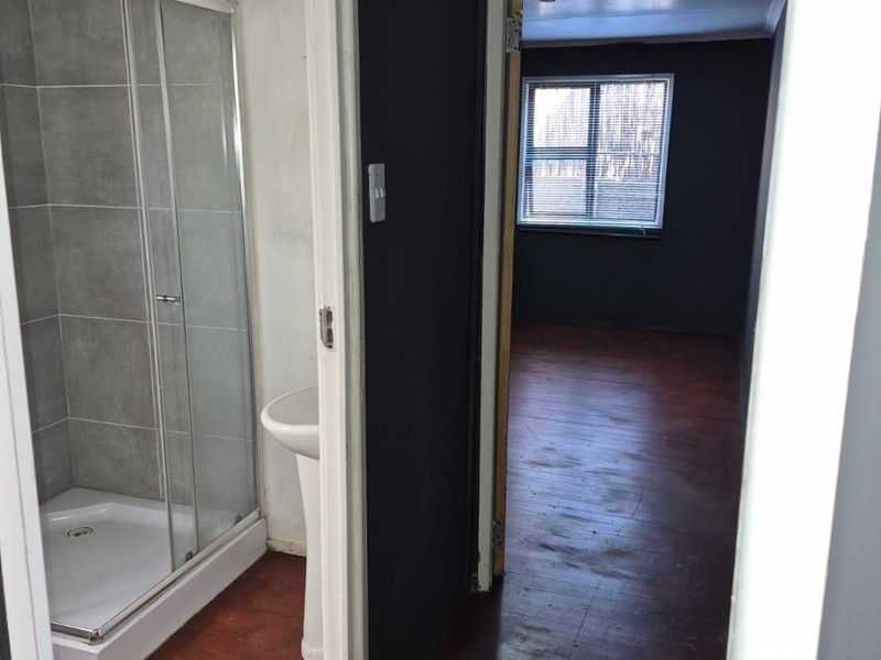 A view from a hallway looking into a bathroom with a shower enclosure and pedestal basin, leading towards an adjacent bedroom.