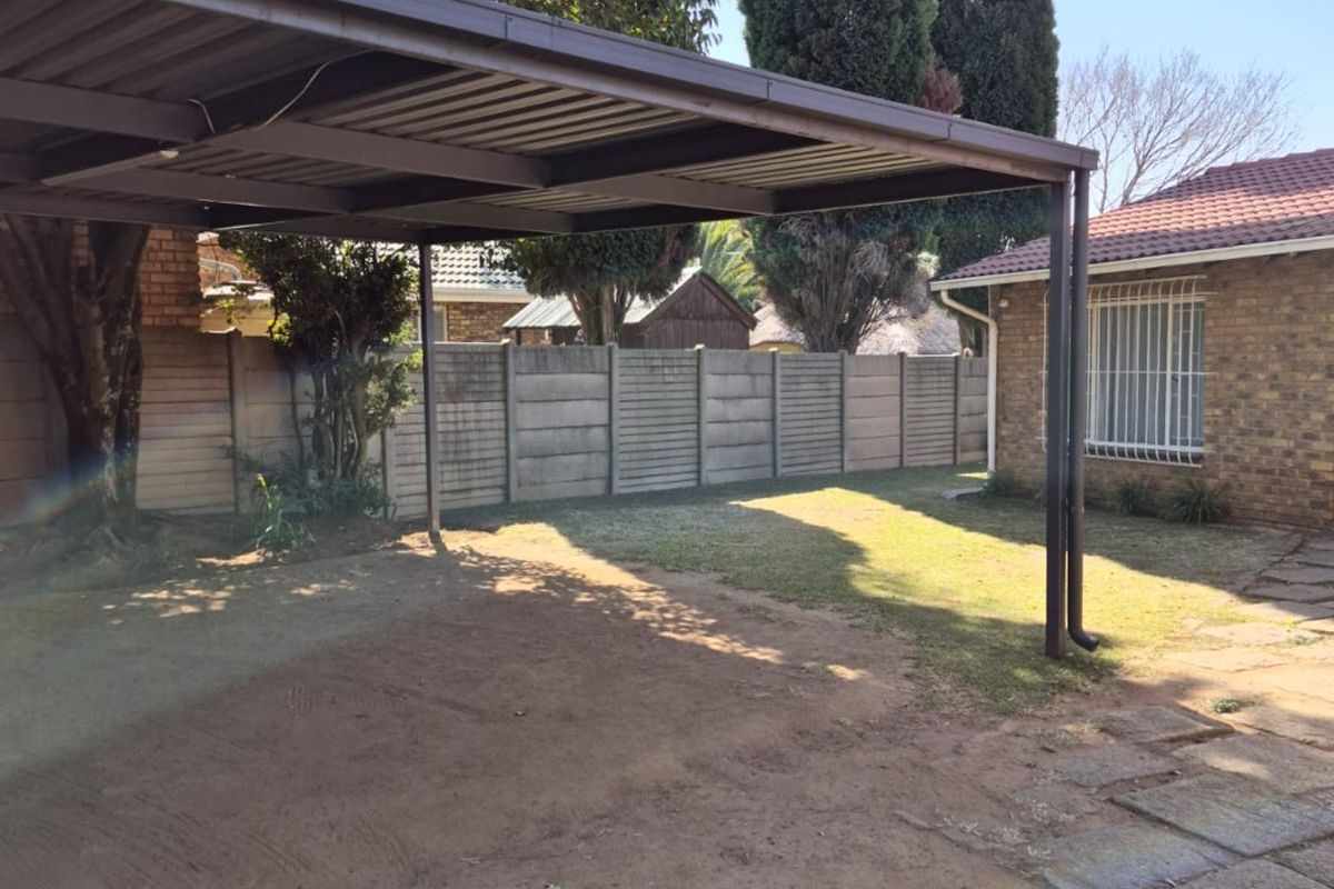Rear exterior area featuring a metal carport structure, brick building facade with security bars, and a precast concrete boundary wall.