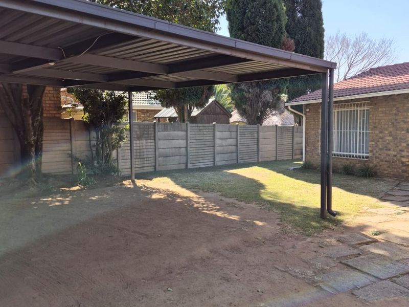Rear exterior area featuring a metal carport structure, brick building facade with security bars, and a precast concrete boundary wall.