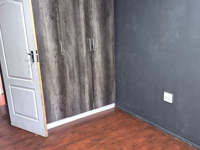 An empty bedroom featuring dark grey walls, wood-look laminate flooring, and a built-in wardrobe with a modern wood-grain finish.
