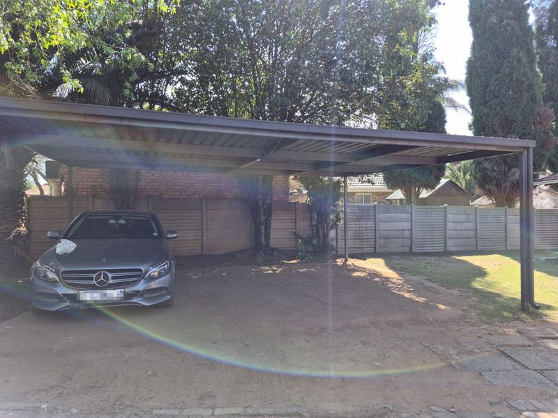 A covered carport structure providing shaded parking space within a residential property boundary.