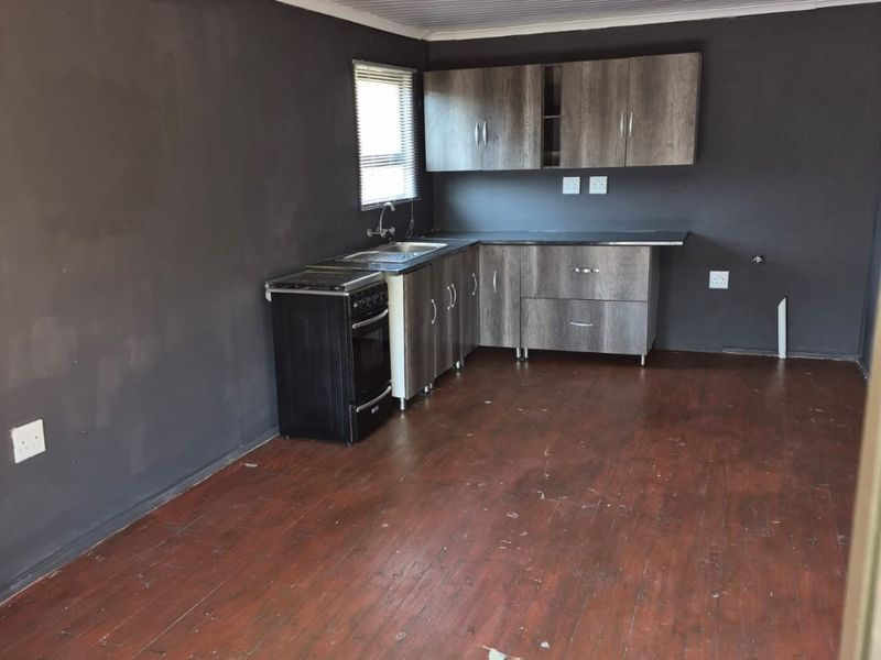 An empty kitchen featuring dark grey walls, wood-look cabinetry, a stainless steel sink, and worn timber flooring, offering a blank canvas for renovation.