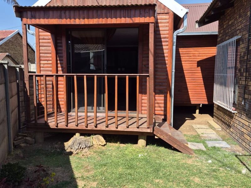 Rear view of a timber-clad structure featuring a raised wooden deck, sliding glass door access, and a small private garden area.