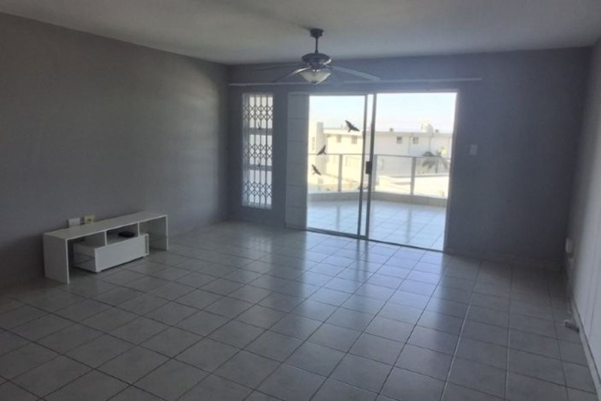 Spacious living area featuring neutral tiled flooring, a ceiling fan, and large sliding glass doors providing access to an outdoor balcony.